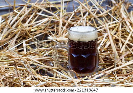 Horizontal image of a glass stein filled with dark draft stout beer on rustic wood and straw