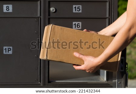 Closeup horizontal front view of female hands putting package into postal mailbox with green grass and sidewalk in background