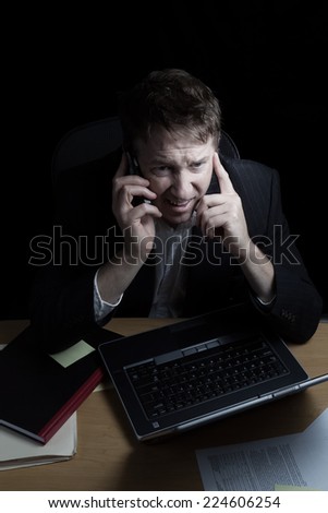 Vertical image of business man, expressing anger while on his cell phone, working late with black background