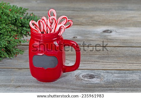 Close up of a red mug filled with holiday candy canes with partial Christmas tree on rustic wood