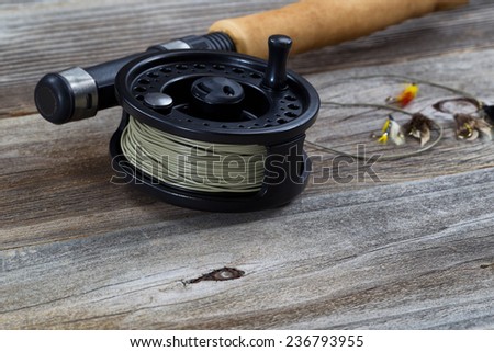 Close up of fly reel, focus on front bottom of reel, with partial cork handled pole and flies blurred out on rustic wooden boards