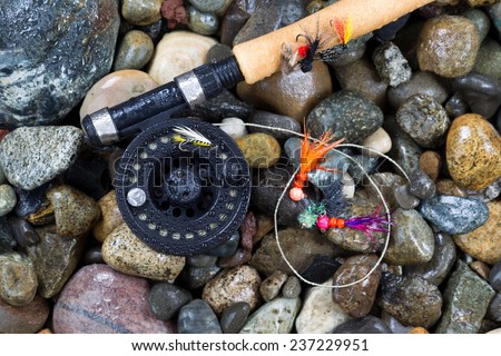 Overhead view of fishing fly reel and assorted flies on wet river bed stones