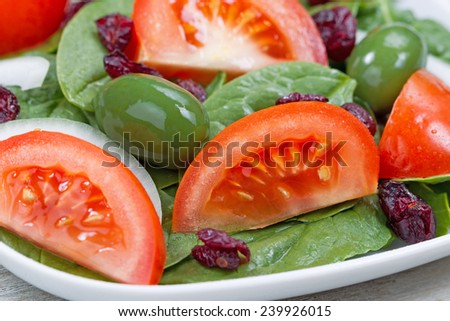 Close up front view, focus on inside tomato and olive, image of a freshly made spinach salad in white plate