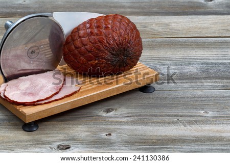 Horizontal image of smoked ham and meat slicer machine on rustic wood