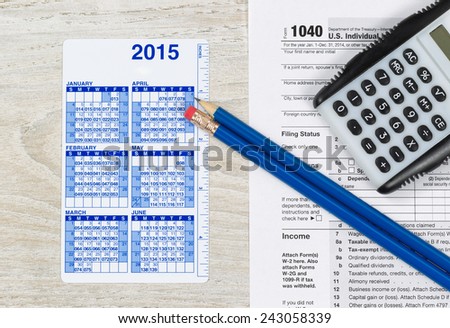 U.S. Tax form 1040 with calculator, calendar and pencils on wooden desktop