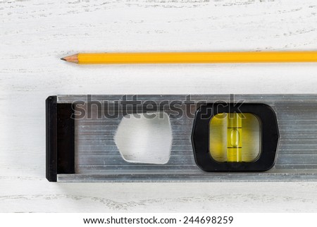 Close up of a metal level tool and yellow pencil on white boards
