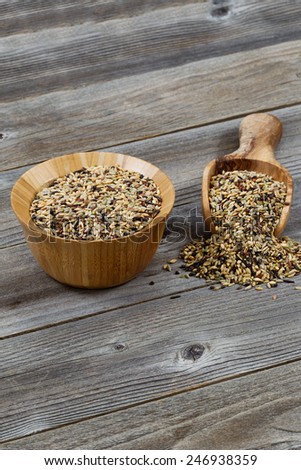 Vertical orientation of a wooden bowl and scoop filled with whole grain rice spilling onto rustic wood