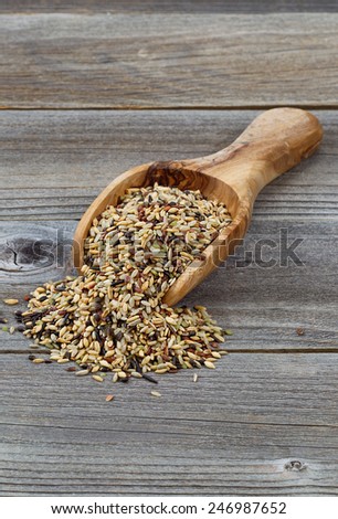 Vertical orientation of a wooden scoop filled with whole grain rice spilling onto rustic wood