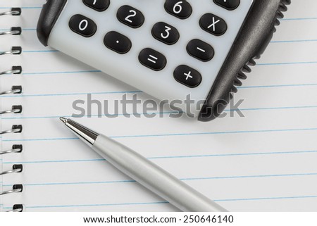 Close up shot of hand held calculator, silver pen and notepad in horizontal layout.