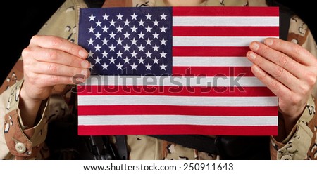 Close up horizontal image of United States of America flag with armed male soldier holding it while on black background.
