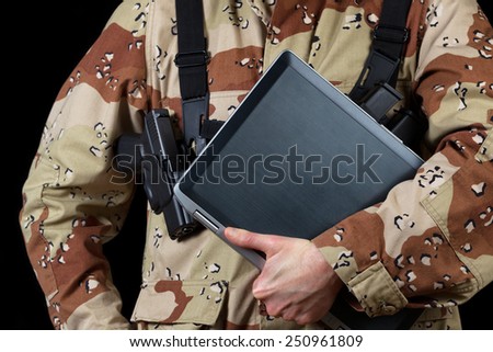 Close up horizontal image of laptop computer with armed male soldier holding it while on black background.