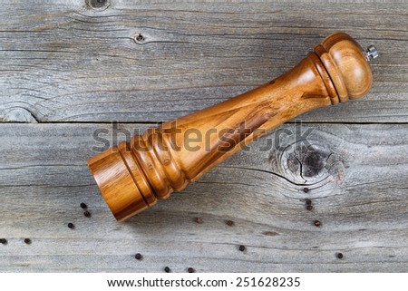 Top view shot of Wooden Pepper Mill with whole black pepper spilled on Rustic Wood