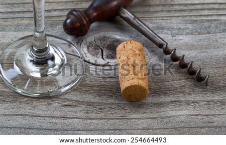 Close up front view of used cork, focus on front part of cork, with antique corkscrew and partial wine glass in background on rustic wood. Horizontal layout.