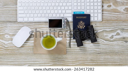 Top view shot of an old white desktop with keyboard, green tea in cup, binoculars, camera, mouse and passport in horizontal format.