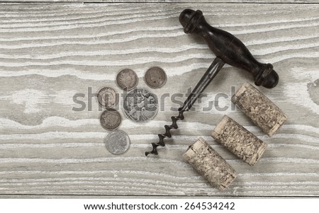Vintage concept of antique corkscrew with three used corks, old coins on rustic wooden boards. Top view angled shot in horizontal format.