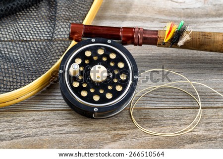 Close up of an antique fly fishing reel, rod, landing net and artificial flies on rustic wood. Layout in horizontal format.