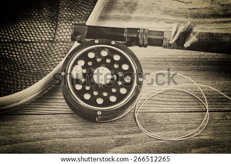 Vintage concept with grain of an antique fly fishing reel, rod, landing net and artificial flies on rustic wood. Close up with layout in horizontal format.