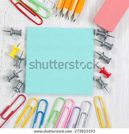 Close up image of school supplies consisting of the following: paper, tacks, paper clips, pencils and eraser on white wood.