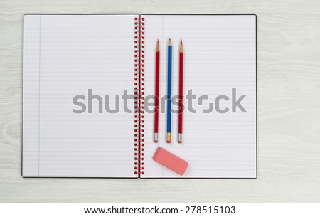 Blank new notepad, in open position, with sharpen pencils and eraser on rustic white desktop.
