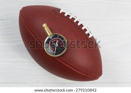 Close up of American football and air pressure gauge on top of ball with rustic white wood underneath.