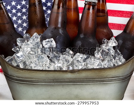 Close up of cold beer and ice in steel tub with American flag in background. Fourth of July holiday concept.