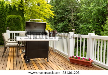 Photo of an open barbecue cooker with cold beer in bucket on cedar wooden patio. Table and colorful trees in background.
