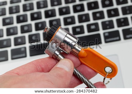 Close up of hand, focus on locking device, holding computer lock with keyboard in background.