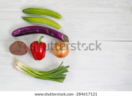 Top view angle shot of fresh vegetables consisting of beet, green onion, yellow onion, red bell pepper, eggplant, and cucumber on white wood. Layout in horizontal format with plenty of copy space.