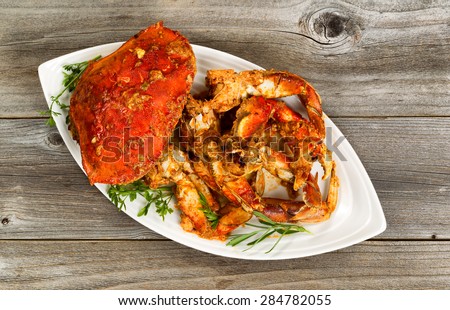 High angled view of freshly cooked crab with spicy sauce and herbs on white serving plate. Rustic wood underneath dish.