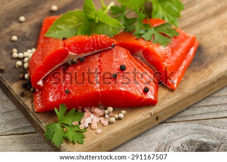 Top view shot of fresh bright red Copper River salmon fillets on cutting board, sea salt and herbs.
