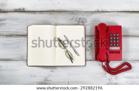 Vintage red phone, notepad, pen and reading glasses on rustic white wooden boards. High angled view.