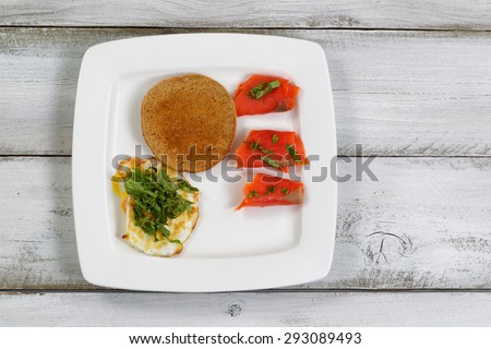 Top view of gourmet breakfast consisting of fresh red salmon, toasted bread with honey, and farmed raised fried egg with chopped basil on top.