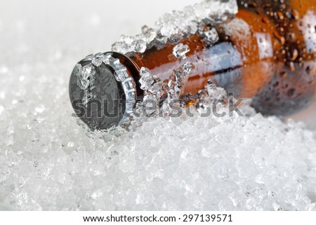 Close up view of a beer bottle neck covered with ice and condensation. Layout in horizontal format. Focus on bottle cap with shallow depth of field.