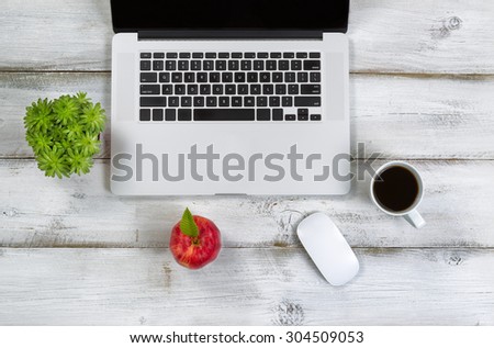 Red apple, coffee, mouse, plant and computer on top of laptop with rustic white desktop.