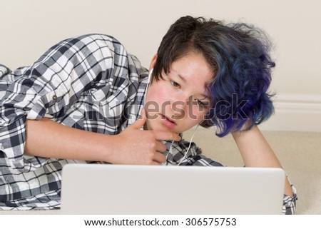 Teen girl thinking while looking at computer and listening to music at home.