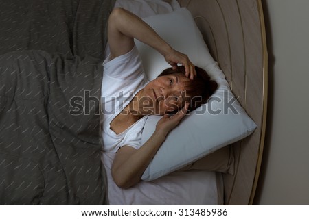 Top view of a senior woman staring at ceiling of bedroom during night time. Insomnia concept.