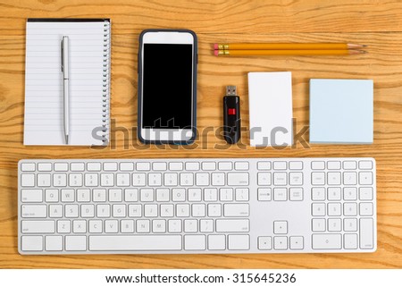 High angled view of a highly organized desktop consisting of computer keyboard, pencils, pen, cell phone, notepad, business cards and thumb drive. Horizontal layout.