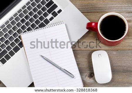 Paper and pen over laptop with coffee and mouse on side of rustic wooden desktop.