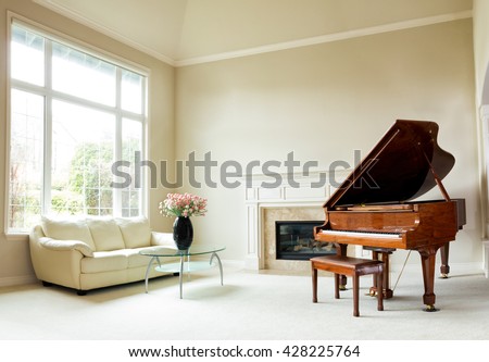 Living room with grand piano, fireplace, sofa and large window with bright daylight coming entering room.