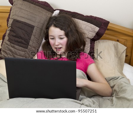 stock photo Asian Preteen with laptop in lap while doing homework in bed