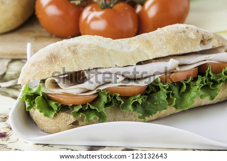 Turkey sub on rustic bread with tomato, bread, lettuce and cheese in the background