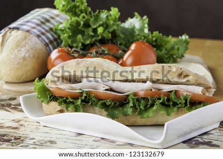 Turkey sub on rustic bread with tomato, bread, lettuce and cheese in the background