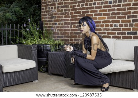 Sexy african american gothic woman smoking. Sitting on a couch outdoor patio, space for text.