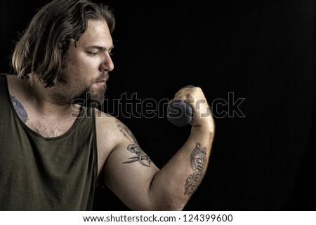 Humorous shot of a large man with tattoos lifting a very small weight