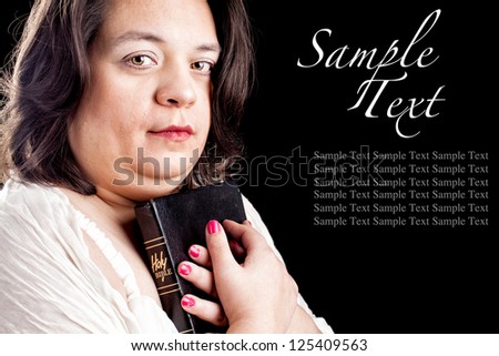 hispanic looking woman in a light dress against a black background holding a bible close to her body as she looks up in thought. Sample text to show how your text can be used.