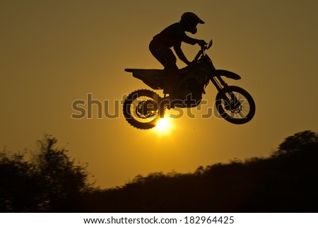 Status of silhouate motocross jumping over the amber light of sunset background.