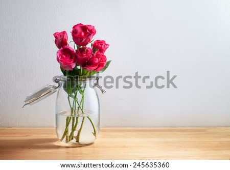Red rose in glass canister on wooden desk top, romantic still life.