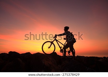 Silhouette of man and his bike on rock mountain with sunrise twilight background.