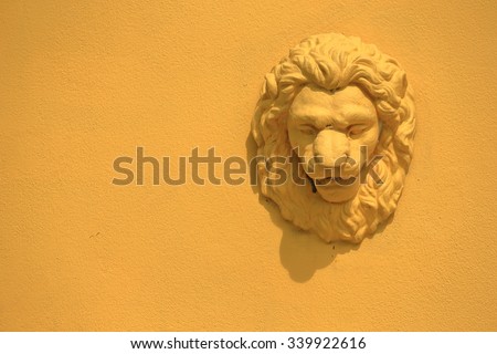 Bas-relief of lion head on yellow wall.