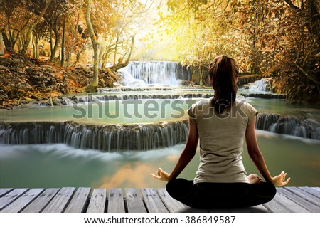 Silhouette of Asian woman yoga on the wooden bridge over waterfall in the autumn forest at the sunrise in the morning. Image create for business, healthcare, sport and lifestyle of people.,